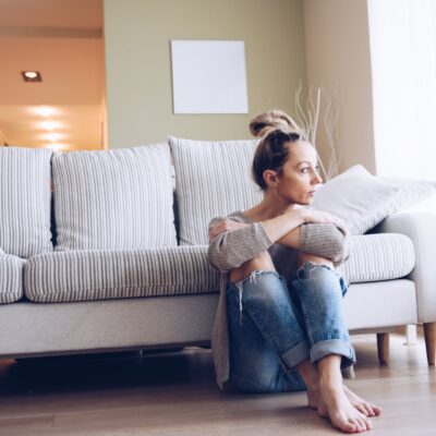 woman with social anxiet at home alone and sitting on floor leaning against couch
